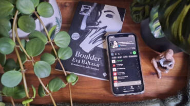Boulder by Eva Baltasar book with a custom play list showing on Spotify phone, surrounded by plants